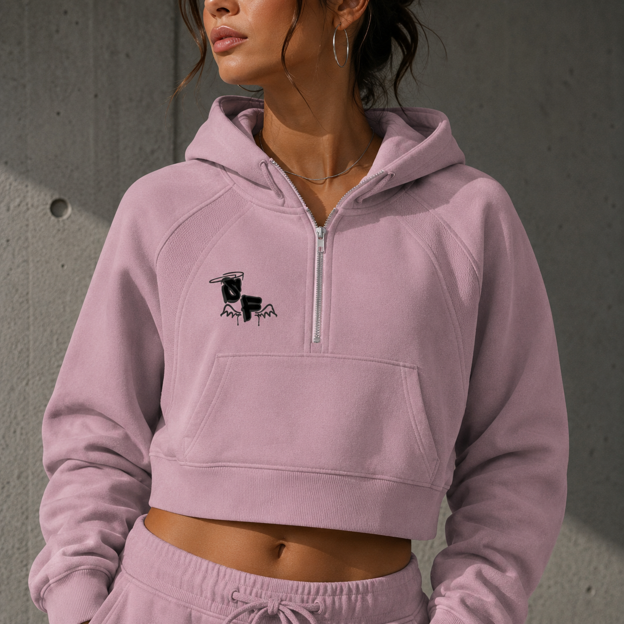 Person wearing a light pink hoodie with a logo on a gray background