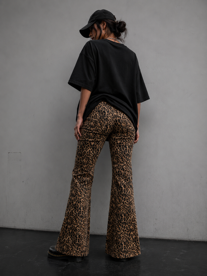 Person wearing a black t-shirt and leopard print pants against a gray wall.