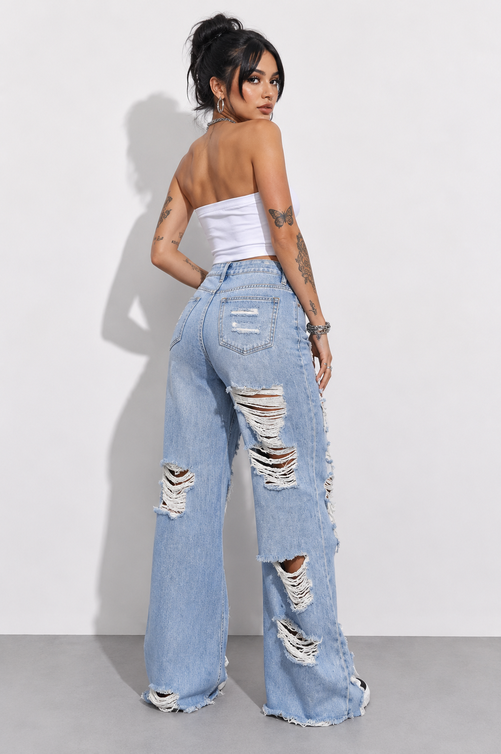 Woman wearing ripped light blue jeans and a white top against a plain background