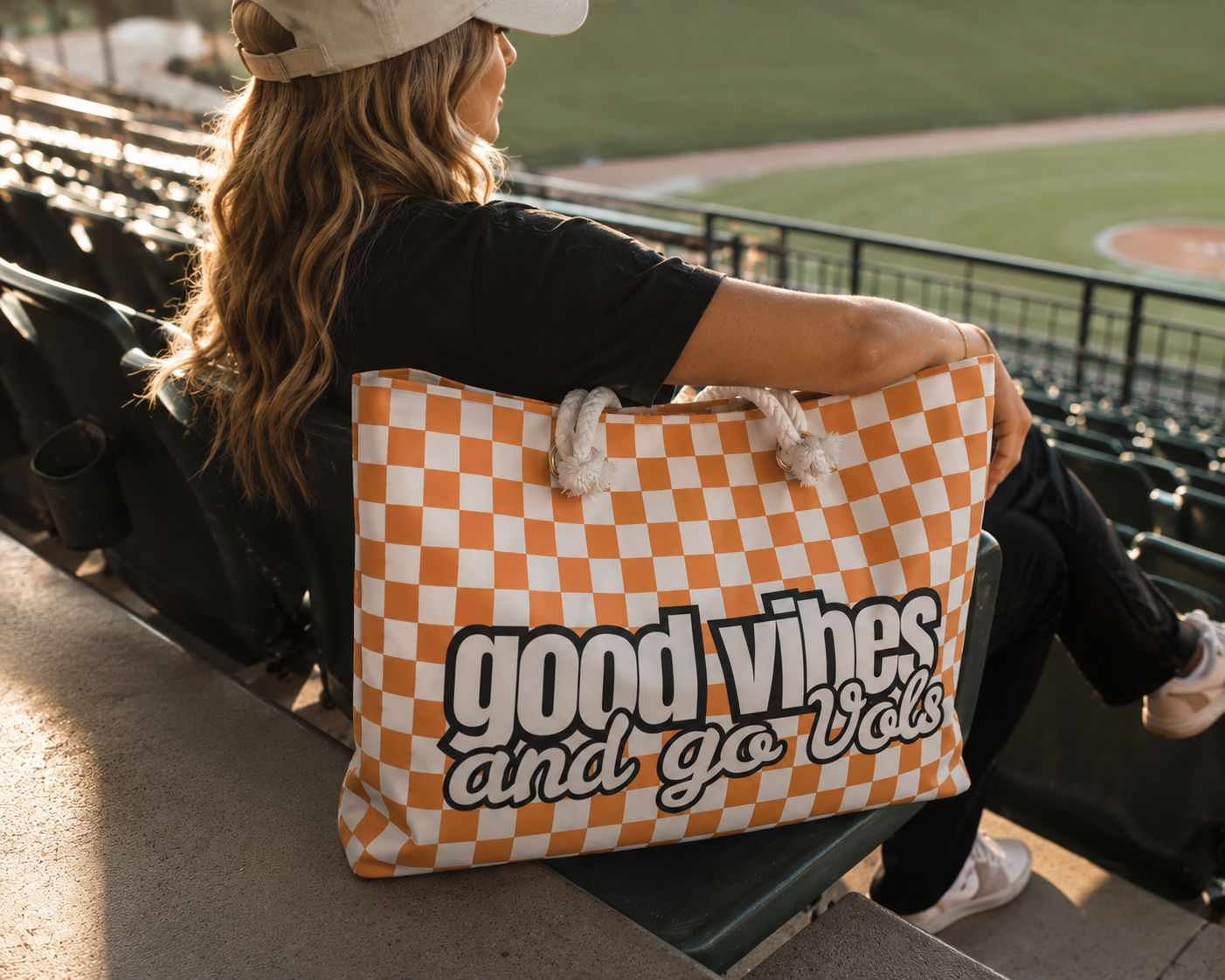 Person sitting in stadium seats with a checkered bag reading 'good vibes and go Vols' at a sports event.