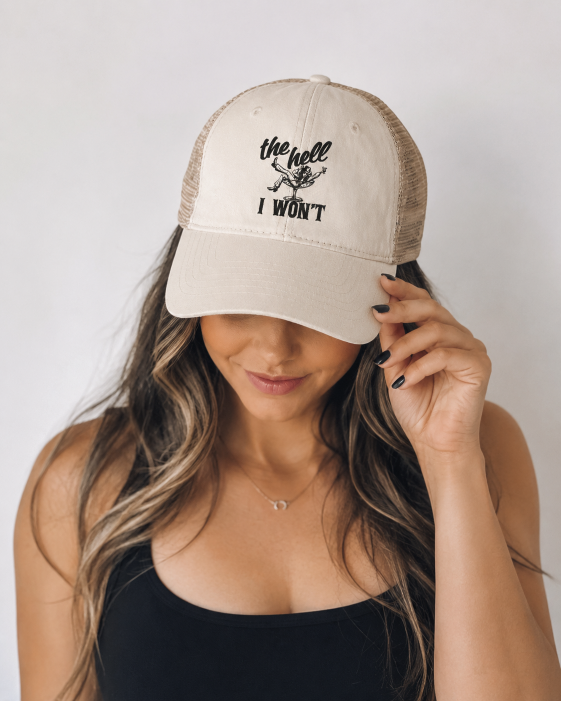 Person wearing a beige cap with text, holding it over their face against a plain background