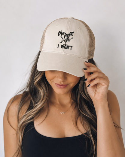 Person wearing a beige cap with text, holding it over their face against a plain background