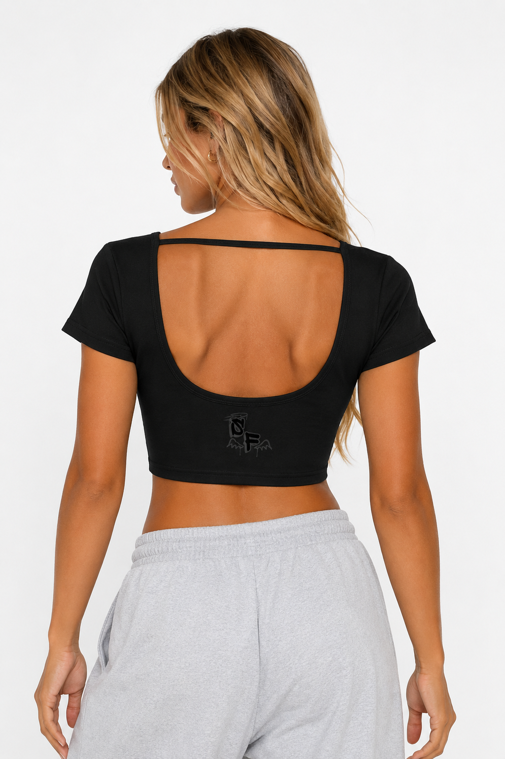 Woman wearing a black crop top with thin straps and gray sweatpants on a white background