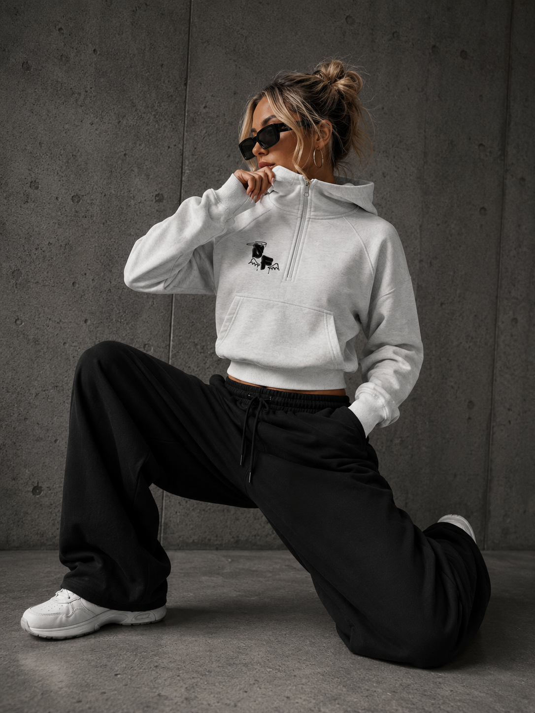 Person wearing a white hoodie with a logo and black pants in a gray room.
