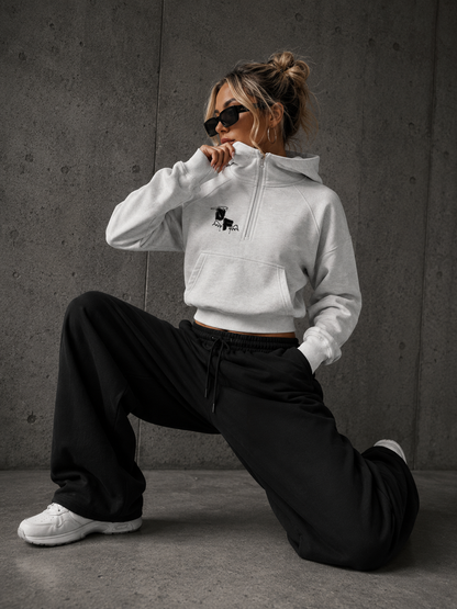 Person wearing a white hoodie with a logo and black pants in a gray room.