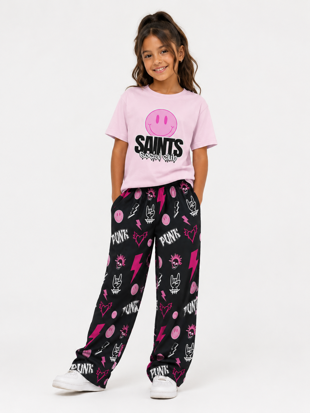 Young girl wearing a pink 'Saints' t-shirt and black pants with pink patterns on a white background