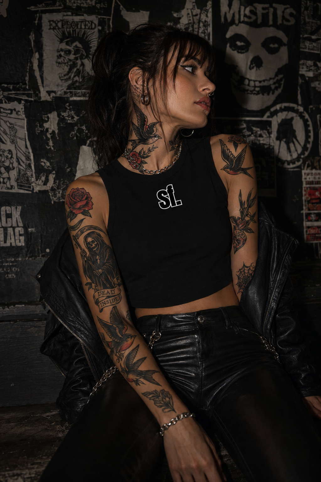 Person with tattoos wearing a black crop top with 'SF' logo against a dark, graphic wall.