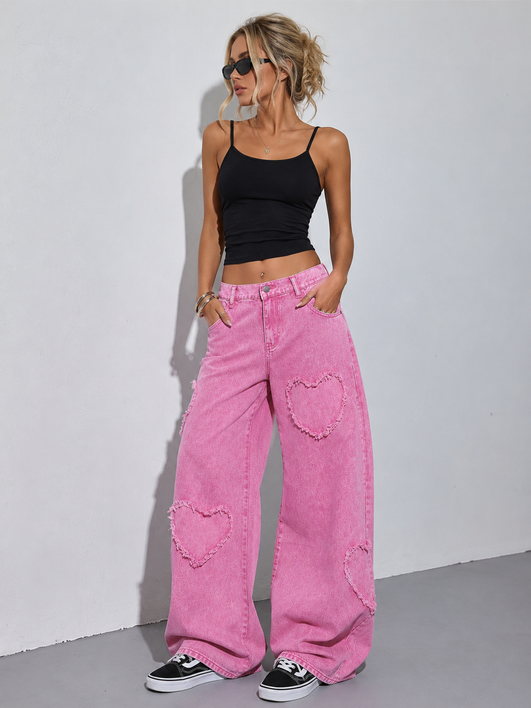 Woman wearing pink jeans with heart designs and a black top against a white background