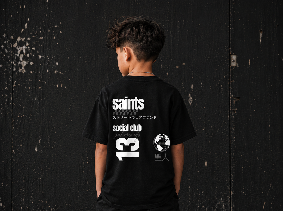 Person wearing a black t-shirt with 'saints social club' text and design on the back against a dark textured wall.